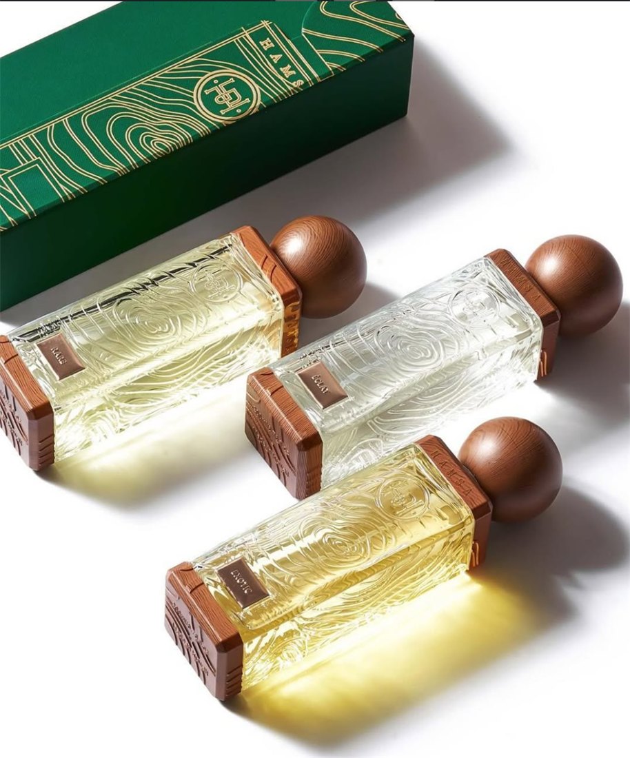 Three Hamsa Exotic bottles with wood-grain glass and wooden cap finials arranged beside their green branded box